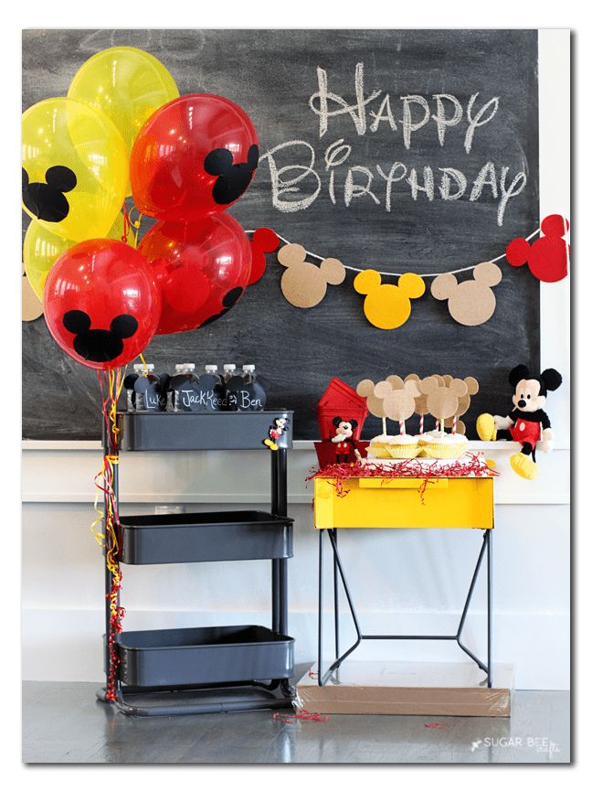 a birthday party with balloons and mickey mouse decorations on the table in front of a chalkboard