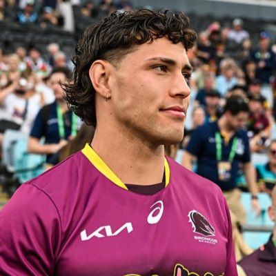 a man in a purple shirt standing next to a stadium full of people and looking off into the distance