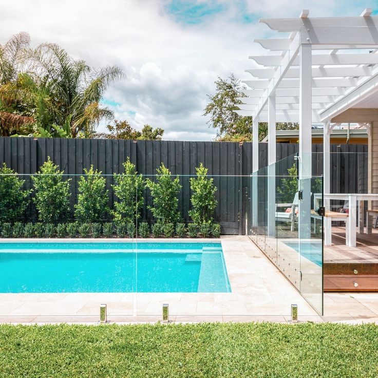 a pool with a glass fence around it and a wooden deck next to the pool