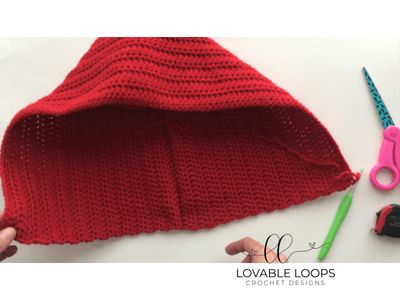 a crocheted red hat with scissors and other crafting supplies next to it