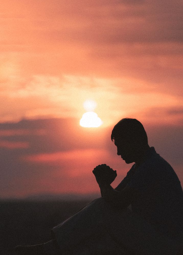 a man sitting on the ground in front of a sunset