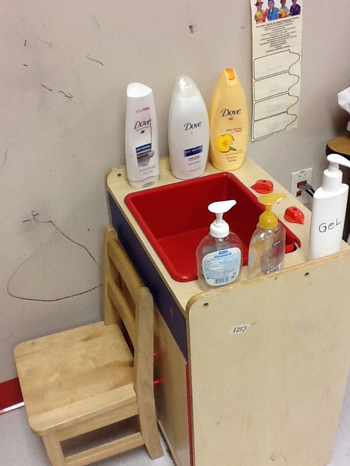 a child's wooden sink and step stool with cleaning products on it in a room