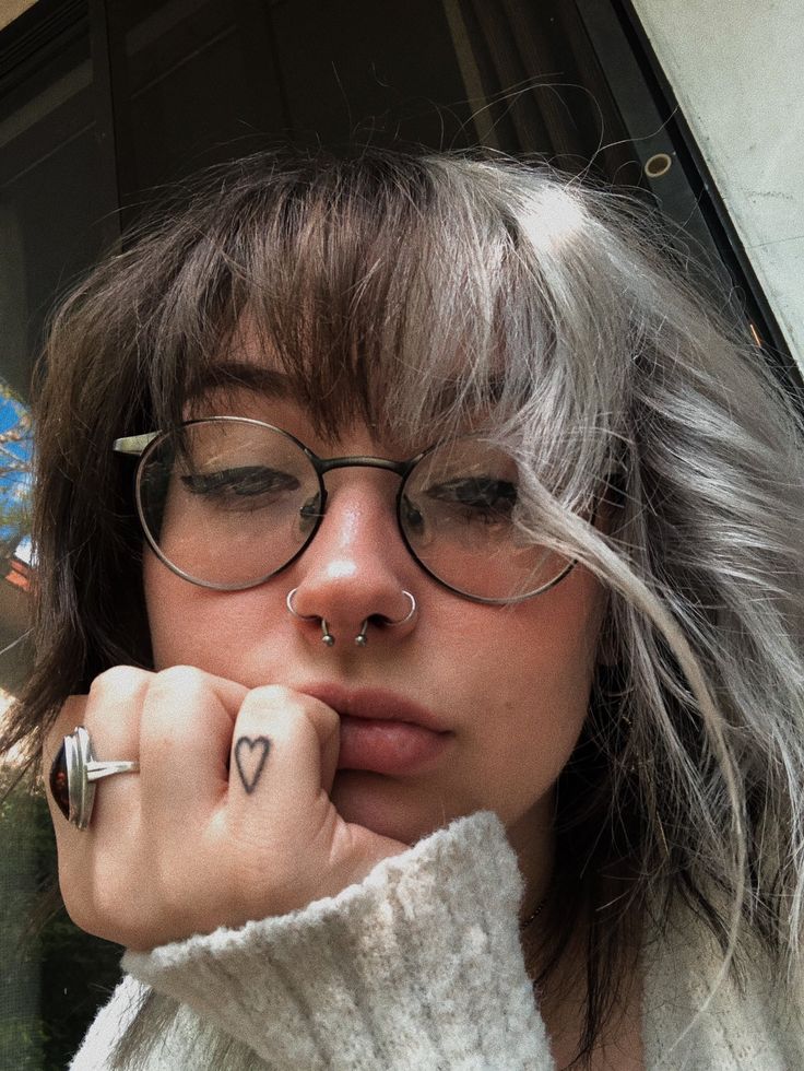 a woman wearing glasses with a heart tattoo on her left hand and nose piercings