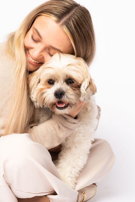 a woman holding a small white dog in her arms and smiling at the camera while sitting down