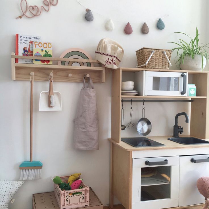 a toy kitchen set up in a playroom with toys on the counter and shelves above it