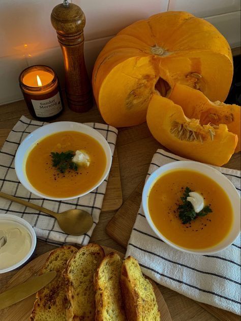 two bowls of soup on a table with bread and pumpkins in the background,