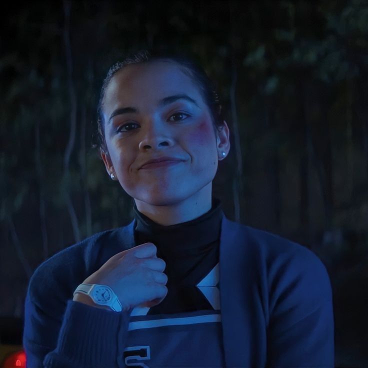 a woman is standing in the dark with her arm around her neck and wearing a watch