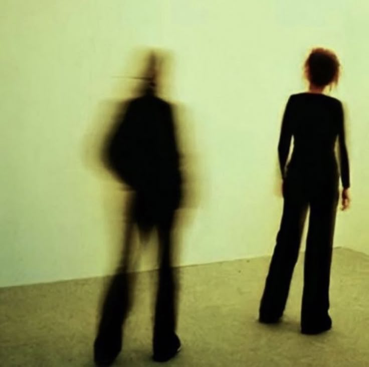 two people standing next to each other in front of a white wall with shadows on it