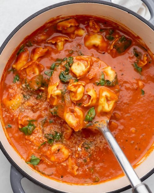 a pot filled with pasta and sauce on top of a white countertop next to a spoon