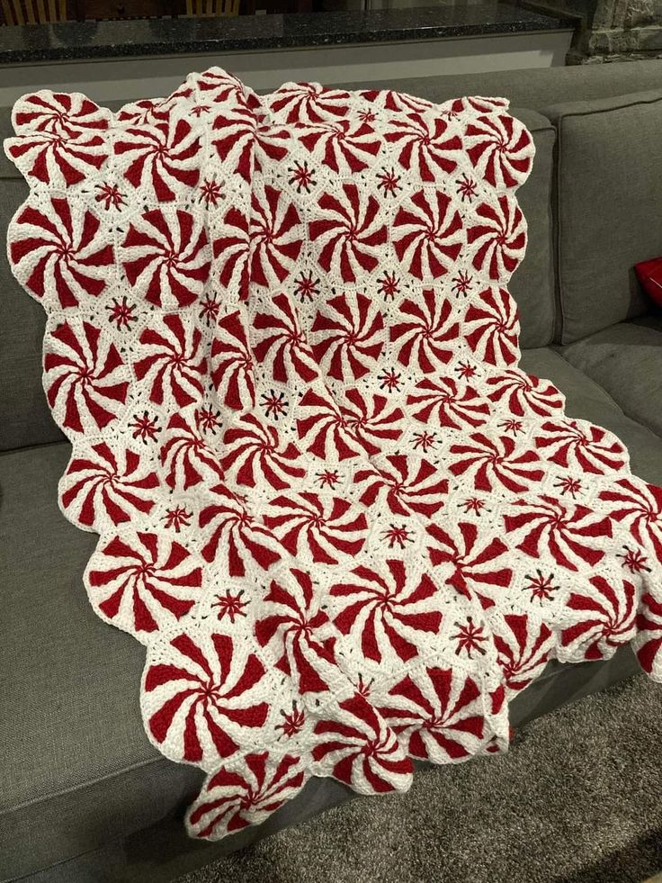 a red and white blanket sitting on top of a couch next to a gray couch