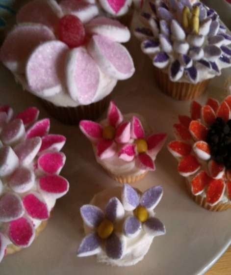 there are many cupcakes decorated with flowers on the white plate and one is pink