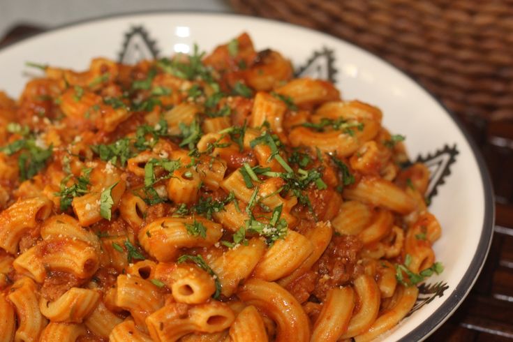 a white plate topped with pasta covered in sauce and parsley on top of a wooden table