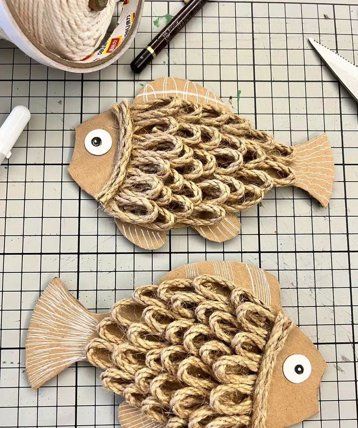 two fish made out of rope sitting on top of a table next to scissors and yarn