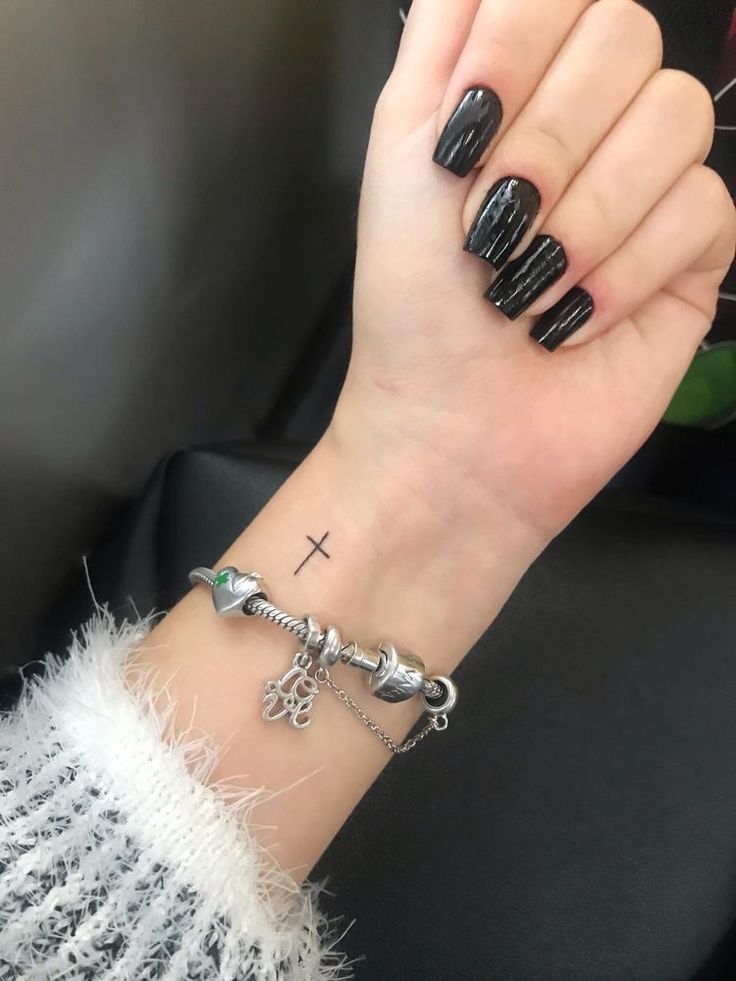 a woman's wrist with black nails and a cross on it