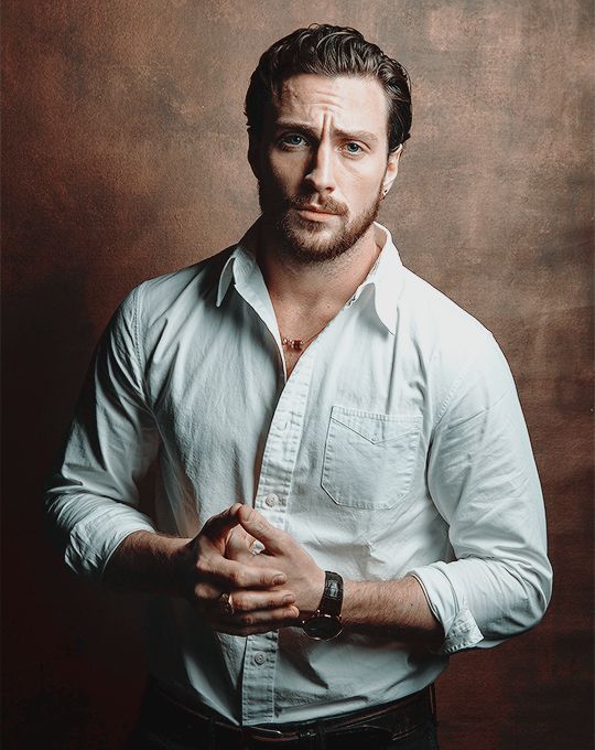 a man standing in front of a wooden wall wearing a white shirt and black pants