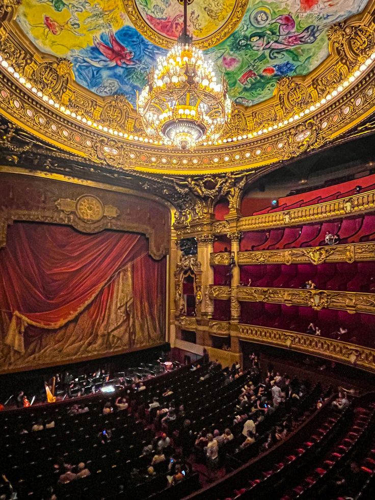 an auditorium filled with lots of people sitting on the stage and looking up at the ceiling