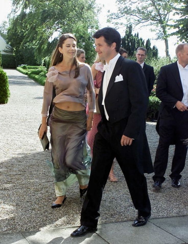 a man and woman are walking down the street with other people in suits behind them