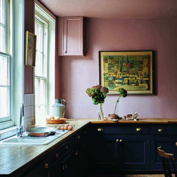 a kitchen with pink walls and black cabinets, an old fashioned painting hangs on the wall