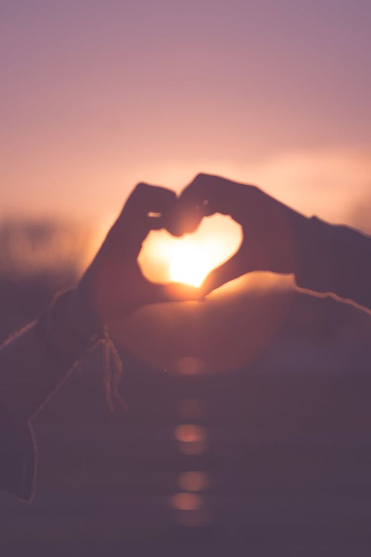 two hands making a heart shape with the sun setting in the back ground behind them