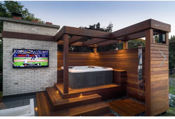 a hot tub sitting on top of a wooden deck next to a brick wall and tv