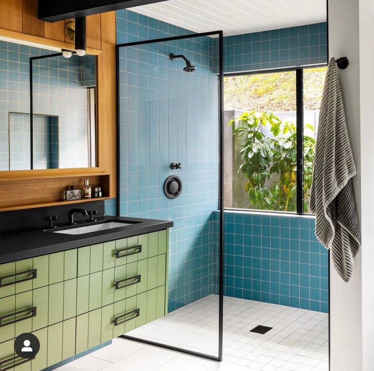 a bathroom with blue and green tiles on the walls, sink, mirror and shower stall