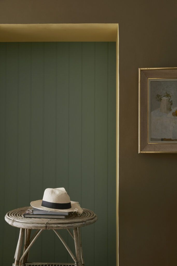 a white hat sitting on top of a wooden stool next to a green painted wall