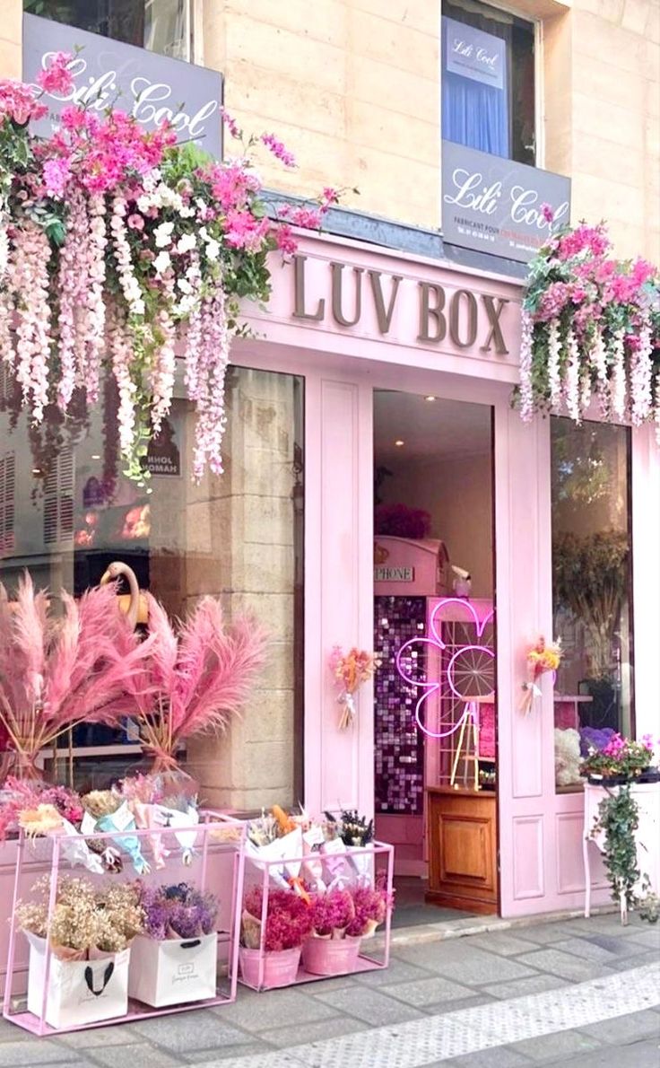 a store front with pink flowers and plants on the outside