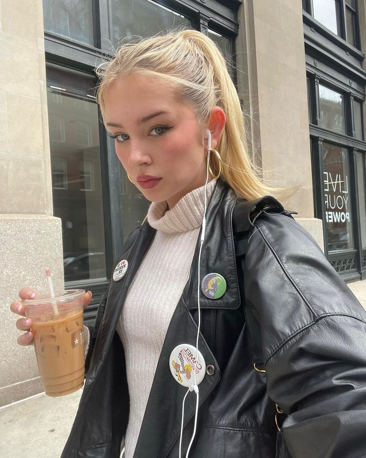 a blonde woman with ear buds and headphones is walking down the street while holding a drink