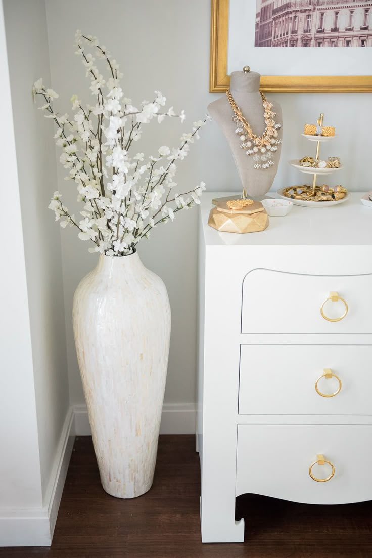 a white vase filled with flowers sitting on top of a table next to a dresser