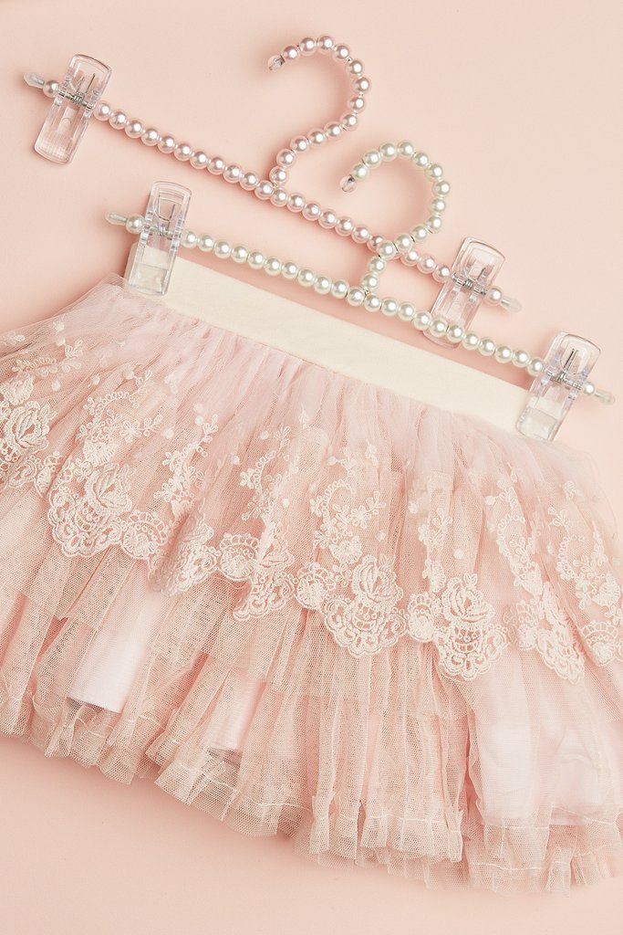 a pink tutu skirt with white lace and pearls hanging from it's hanger