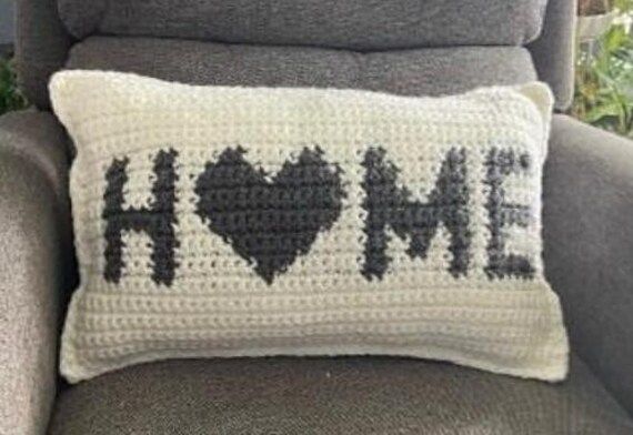 a crocheted pillow with the word home written on it in black and white