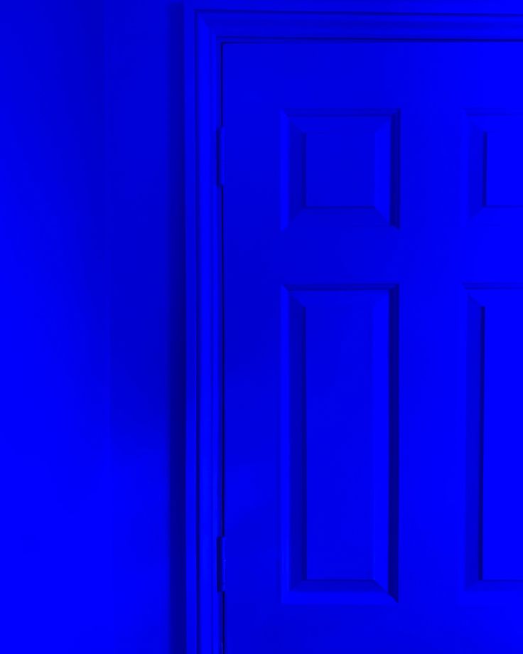 a blue door in a room with a black cat sitting on the floor next to it