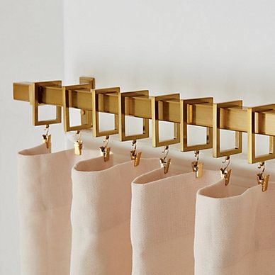 four gold hooks are hanging on the side of a curtain rod in front of a white wall