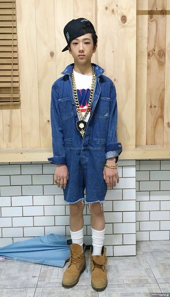 a young boy in overalls and hat standing next to a wall with wood paneling