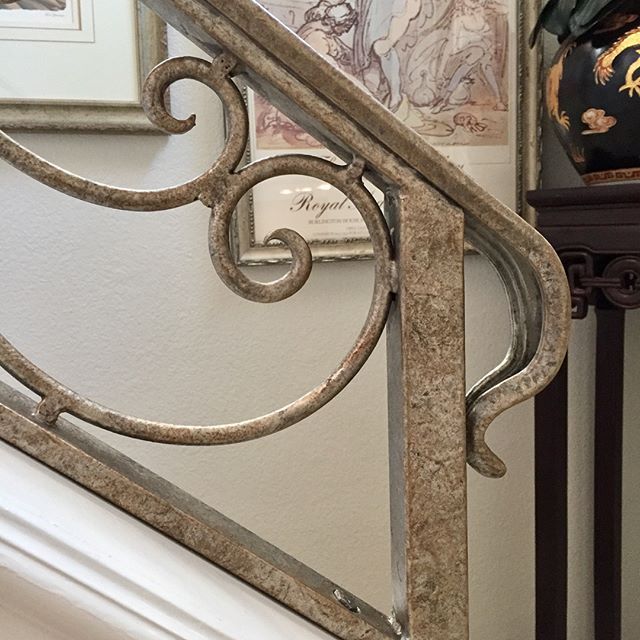 an ornate iron stair railing next to a clock and framed pictures on the wall behind it