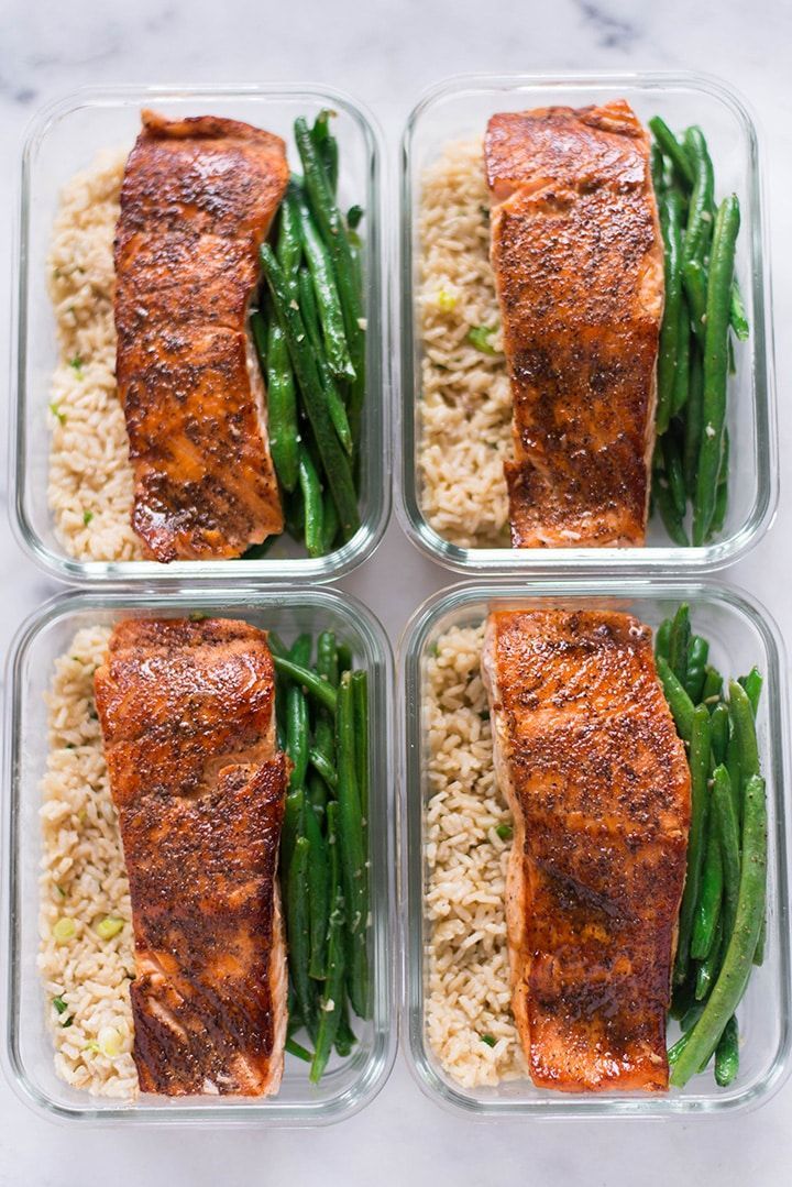 four glass containers filled with salmon, green beans and rice on top of a marble counter