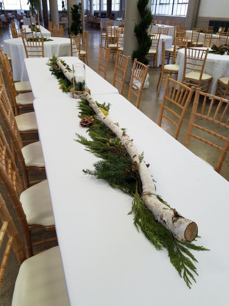 the table is set up with white linens and greenery