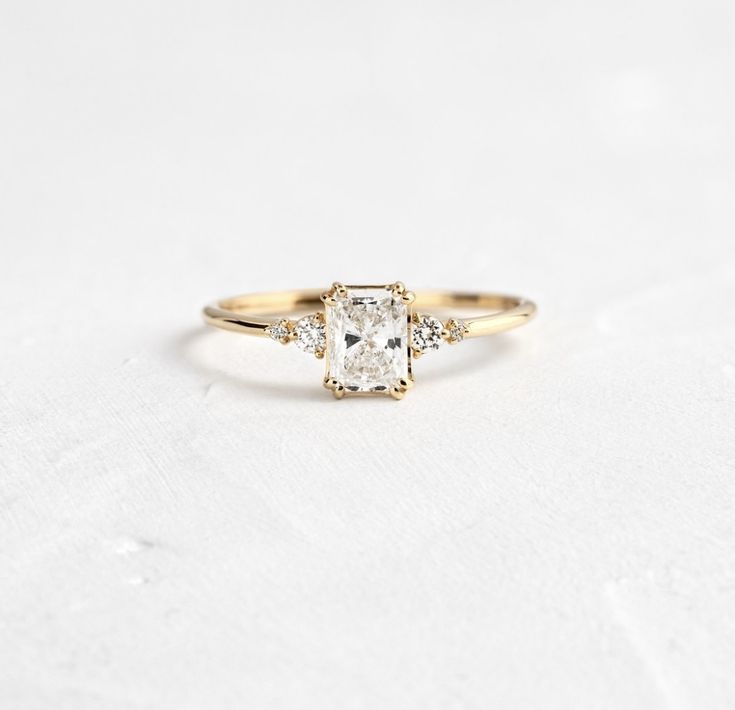 an engagement ring with two diamonds on the side and one diamond in the middle, sitting on top of a white surface