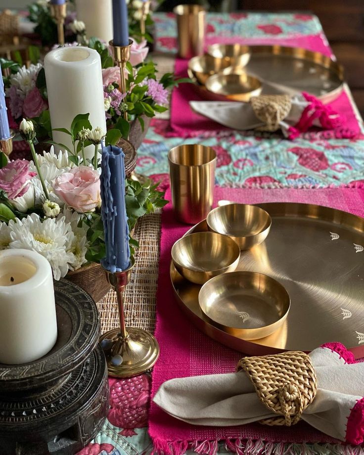 the table is set with gold dishes and pink napkins, candles, and flowers