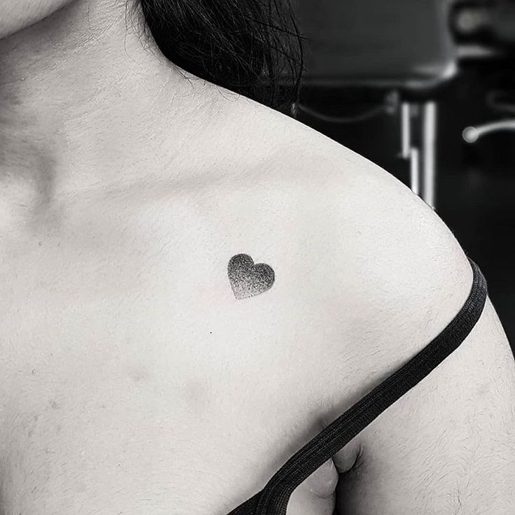 a black and white photo of a woman's chest with a small heart tattoo on it