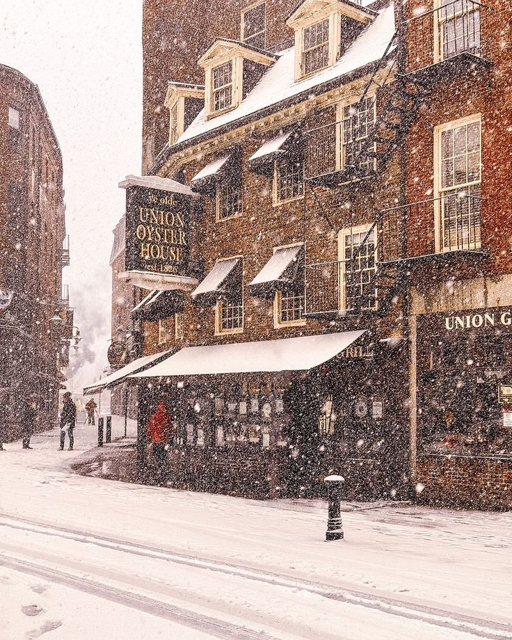 people are walking in the snow on a city street with buildings and shops covered in snow