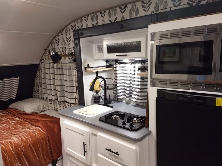 a small kitchenette with sink, stove and microwave in a tiny room that also has a bed