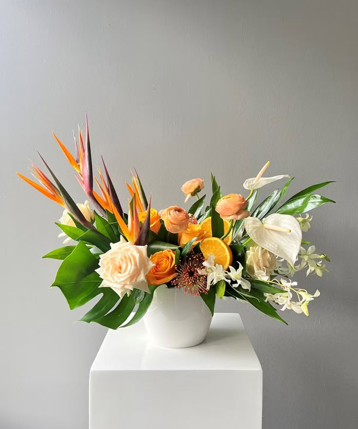 an arrangement of flowers in a white vase on top of a pedestal against a gray wall