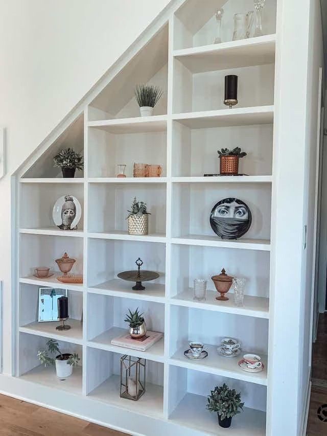 a white bookcase filled with lots of shelves next to a stair case in a house