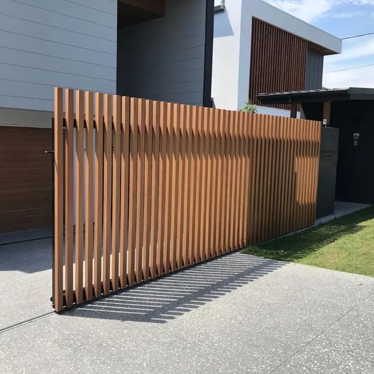 a large wooden fence in front of a house with two garage doors on each side