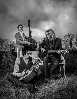 three men sitting on a bench with guitars in their hands and one man playing the guitar