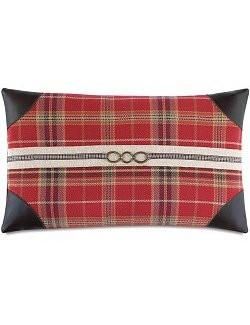 a red and black plaid pillow with an oval buckle on the front, along with leather trim