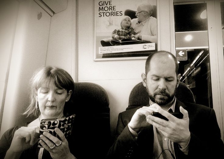 two people sitting next to each other while looking at their cell phones