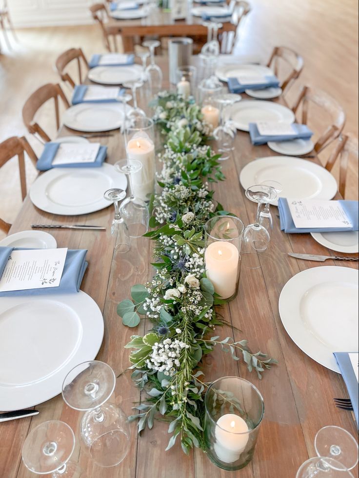 Simplistic and organic greenery garland with pillar candles and accented by dusty blue napkins. Farmhouse Table Florals Wedding, White Dusty Blue Wedding, Simple Dusty Blue Wedding, Wedding Table Decor Dusty Blue, Dusty Blue Wedding Centerpieces Simple, Simple Dusty Blue Centerpieces, Slate Blue And Light Blue Wedding, Dusty Blue Table Decor Wedding, Dusty Blue Wedding Tables