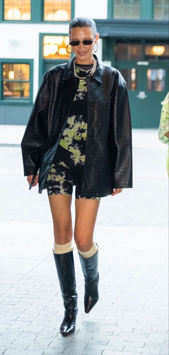 a woman walking down the street wearing black boots and a dress with flowers on it